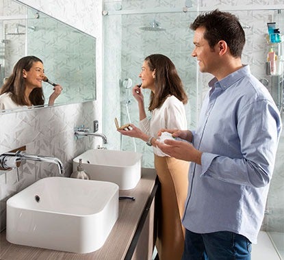 Casal jovem numa casa de banho moderna olha para o espelho com iluminação junto de um móvel com lavatórios