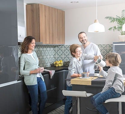 Família com pai, mãe e dois filhos numa cozinha em tons de cinzento junto ao balcão a cozinhar