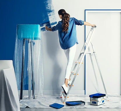 Rapariga em cima de escadote pinta parede branca com tinta azul forte