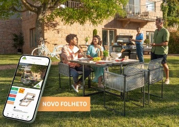 ambiente num jardim, com uma família a comer uma refeição num conjunto de mesa e cadeiras de exterior e a grelhar comida num barbecue a gás