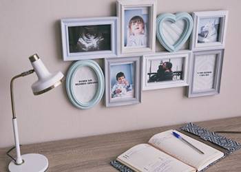 Moldura multifotos com várias fotografias, junto a um candeeiro de mesa e livro