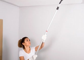 Senhora a pintar o teto com tinta branca numa sala em renovação