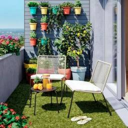Varanda com horta vertical, chão revestido com relva artificial, vasos coloridos e mobiliário de jardim - cadeiras e mesa de apoio 