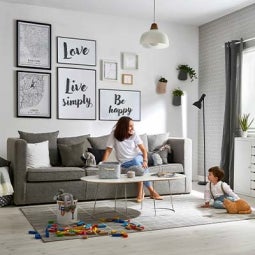 mãe e filho em sala de estar, junto a parede decorada com várias moduldas, candeeiro suspenso e tapete