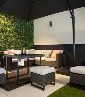 Ambiente elegante com conjunto de mobiliário de jardim sofisticado de vime escuro com almofadas brancas e um chapéu de sol grande preto  