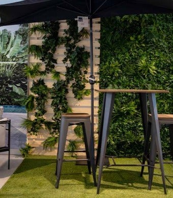 Ambiente com parede forrada com jardim vertical, chão com relva artificial e uma mesa e banco altos